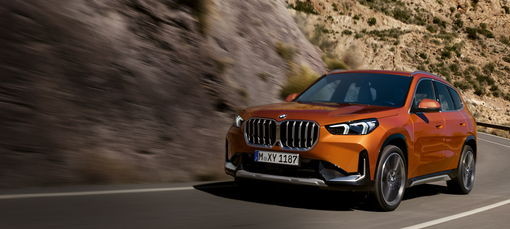 BMW X1 U11 xLine Utah orange metallic sett skrått forfra kjørende på landevei