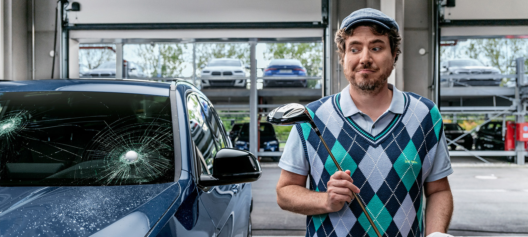 Mann som holder en golfkølle ved siden av en BMW som har blitt truffet av en golfball i frontruten.